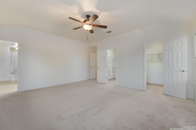 unfurnished bedroom with vaulted ceiling, connected bathroom, a spacious closet, light colored carpet, and ceiling fan