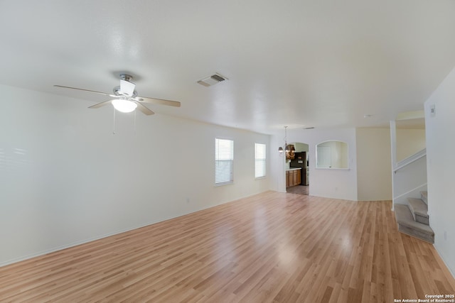 unfurnished living room with ceiling fan with notable chandelier and light hardwood / wood-style flooring