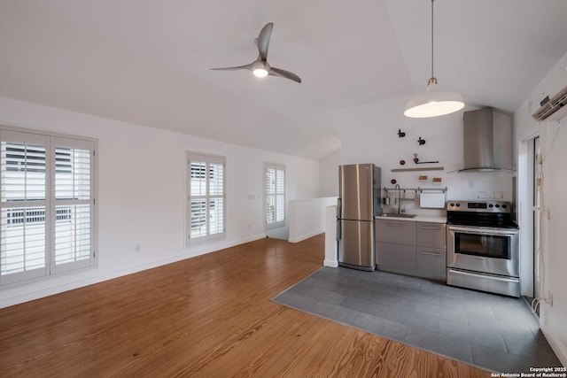 kitchen with wall chimney range hood, sink, gray cabinetry, stainless steel appliances, and vaulted ceiling