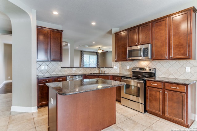 kitchen featuring light tile patterned flooring, a kitchen island, sink, dark stone countertops, and stainless steel appliances