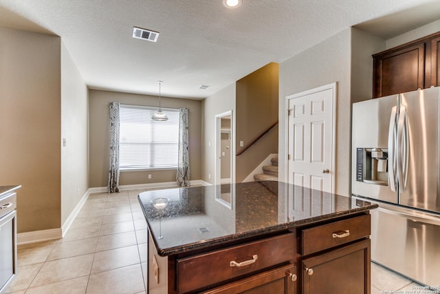 kitchen featuring a kitchen island, dark stone countertops, light tile patterned floors, and stainless steel fridge with ice dispenser