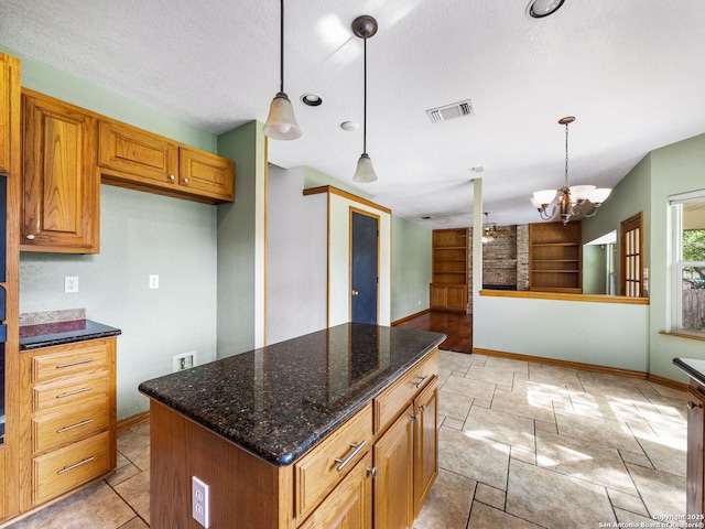 kitchen with dark stone counters, hanging light fixtures, a center island, a textured ceiling, and an inviting chandelier