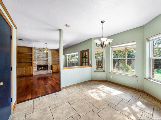 unfurnished dining area with a brick fireplace, ceiling fan with notable chandelier, built in features, and a textured ceiling