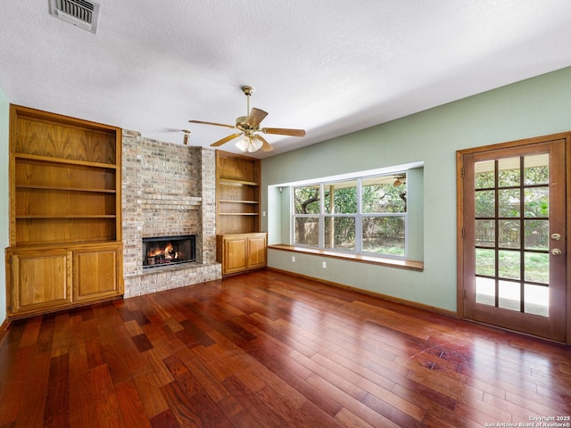 unfurnished living room with ceiling fan, a fireplace, a textured ceiling, dark hardwood / wood-style flooring, and built in shelves