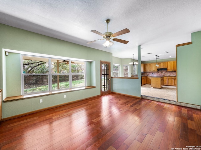 unfurnished living room with ceiling fan with notable chandelier, light hardwood / wood-style floors, and a textured ceiling