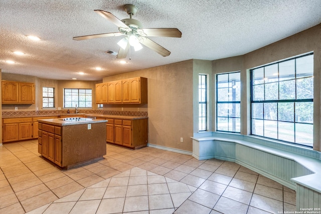 kitchen with light tile patterned floors, a center island, a textured ceiling, and ceiling fan