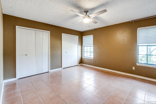 unfurnished bedroom featuring two closets, a textured ceiling, and light tile patterned floors