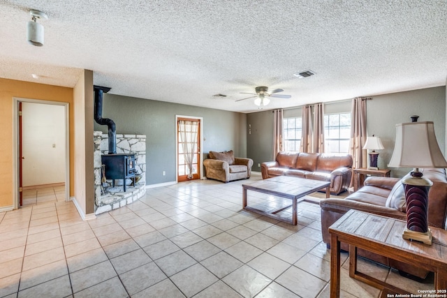 living room featuring a wood stove, light tile patterned floors, a textured ceiling, and ceiling fan