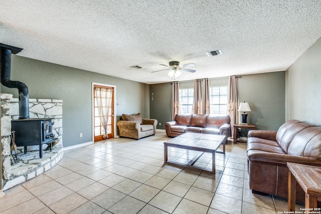 tiled living room featuring a wood stove, a textured ceiling, and ceiling fan