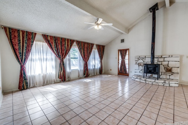 unfurnished living room featuring light tile patterned floors, ceiling fan, beam ceiling, a textured ceiling, and a wood stove