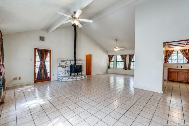 unfurnished living room with beamed ceiling, ceiling fan, a wood stove, and light tile patterned floors