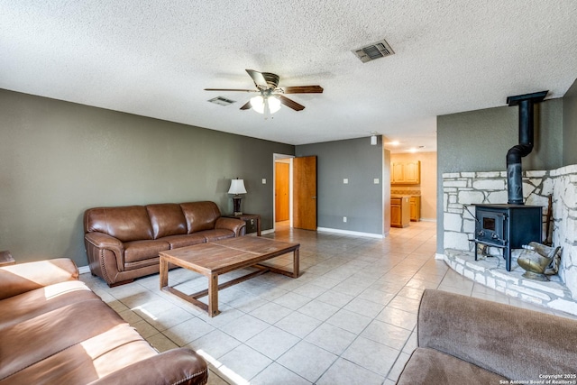 tiled living room featuring a textured ceiling, ceiling fan, and a wood stove