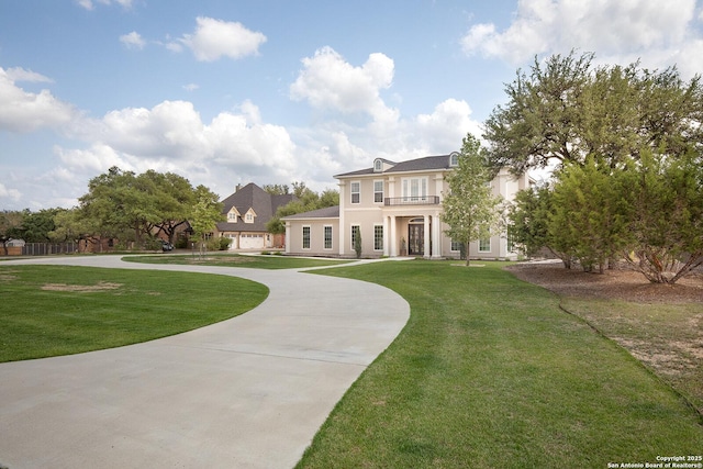 view of front of home featuring curved driveway, a balcony, stucco siding, and a front lawn