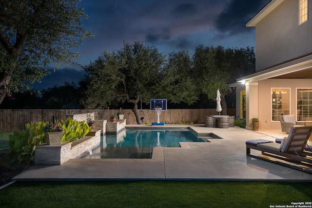 pool at night featuring a patio and a fenced backyard