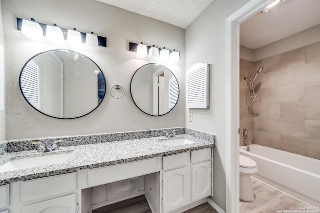 full bathroom with tiled shower / bath, hardwood / wood-style flooring, vanity, toilet, and a textured ceiling