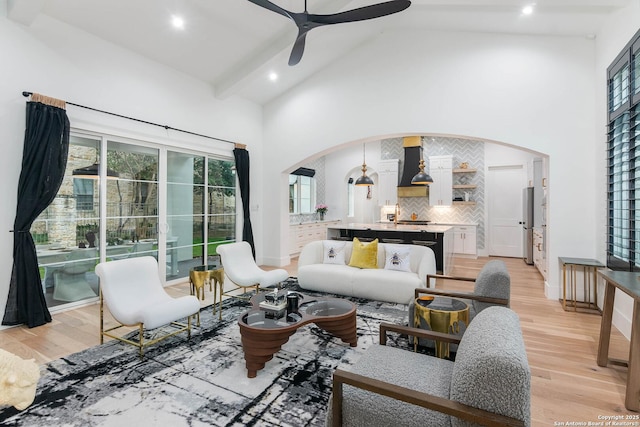 living room with ceiling fan, beam ceiling, high vaulted ceiling, and light wood-type flooring