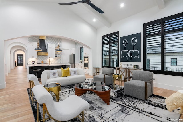 living room featuring beamed ceiling, ceiling fan, high vaulted ceiling, and light hardwood / wood-style flooring