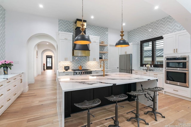 kitchen featuring appliances with stainless steel finishes, pendant lighting, white cabinetry, sink, and a large island with sink