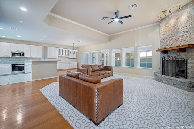 living room featuring ornamental molding, a fireplace, ceiling fan with notable chandelier, and light wood-type flooring