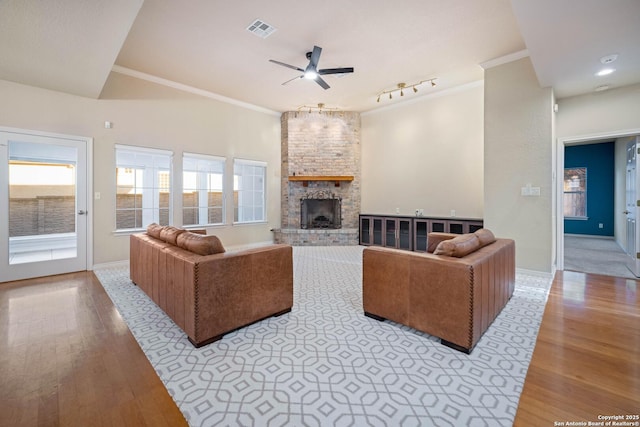 living room featuring a stone fireplace, light hardwood / wood-style flooring, ornamental molding, and ceiling fan