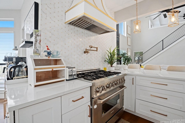 kitchen with stainless steel stove, ceiling fan, light stone countertops, white cabinets, and custom exhaust hood