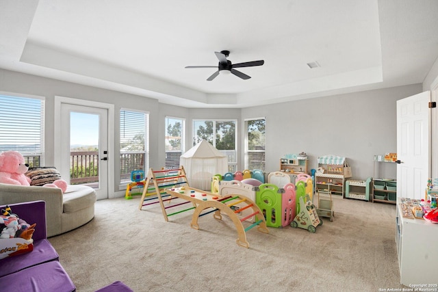 recreation room with light carpet, a tray ceiling, and ceiling fan