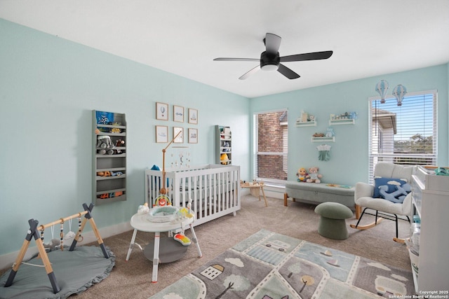 carpeted bedroom with a crib and ceiling fan