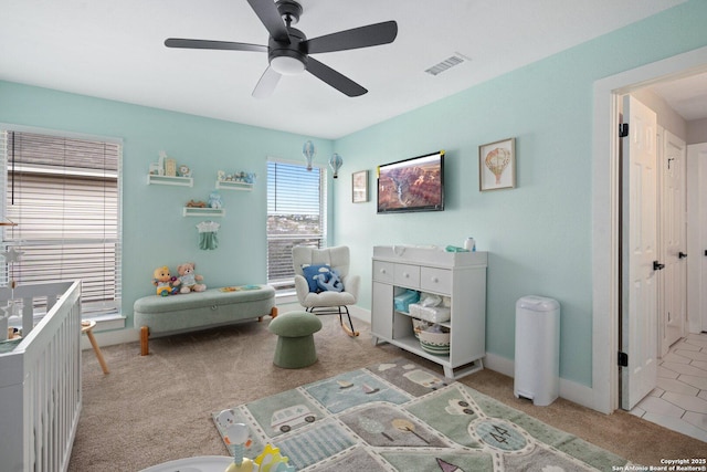 bedroom with a crib, light colored carpet, and ceiling fan