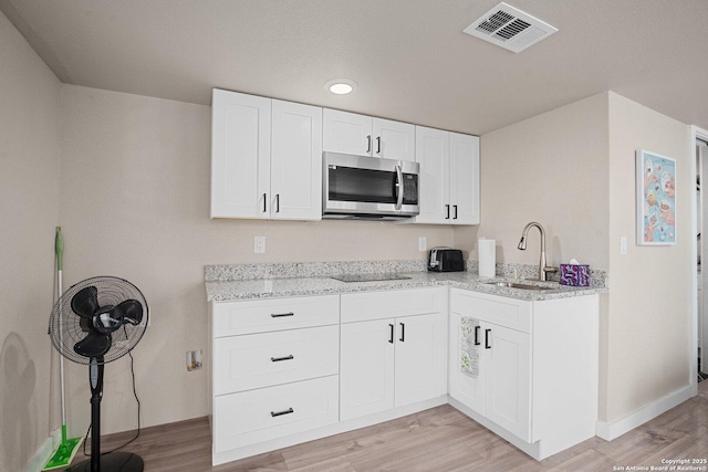 kitchen with light stone counters, sink, light hardwood / wood-style flooring, and white cabinets