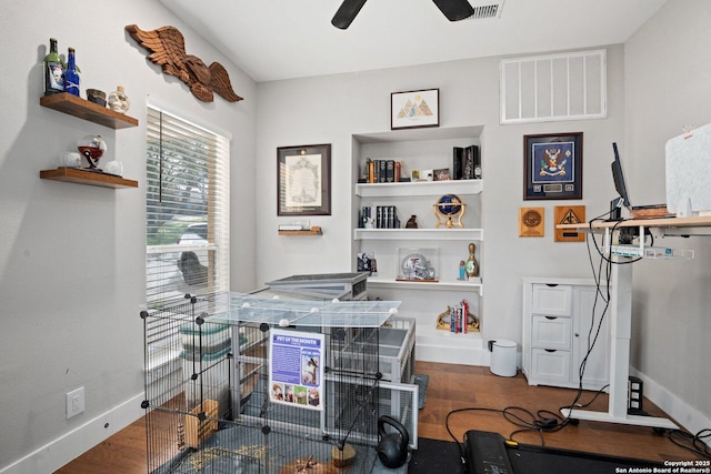 home office with built in shelves, dark wood-type flooring, and ceiling fan