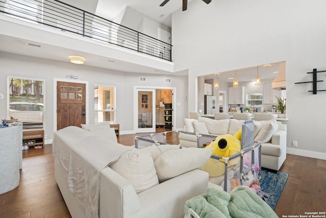 living room with plenty of natural light, dark wood-type flooring, ceiling fan, and a towering ceiling