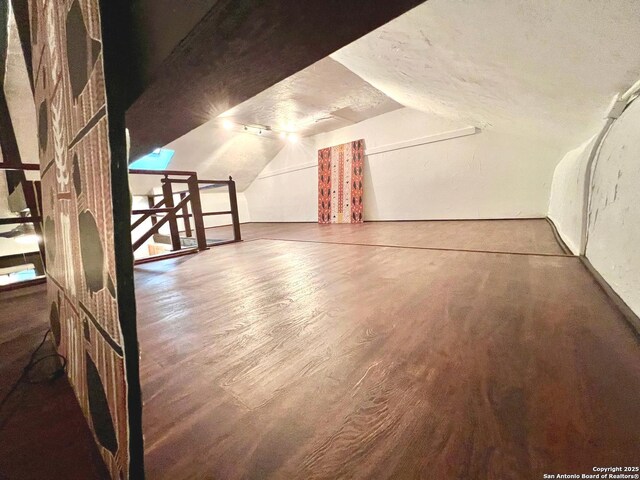 bonus room featuring dark wood-type flooring, vaulted ceiling, and a textured ceiling