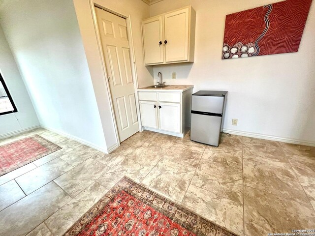 kitchen featuring sink, stainless steel refrigerator, and white cabinets