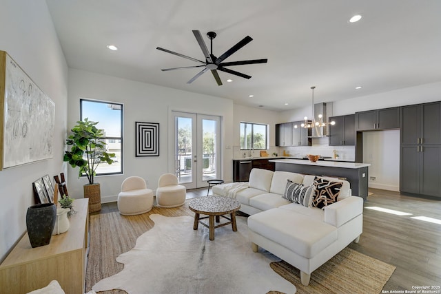 living room with ceiling fan with notable chandelier, light hardwood / wood-style floors, and french doors