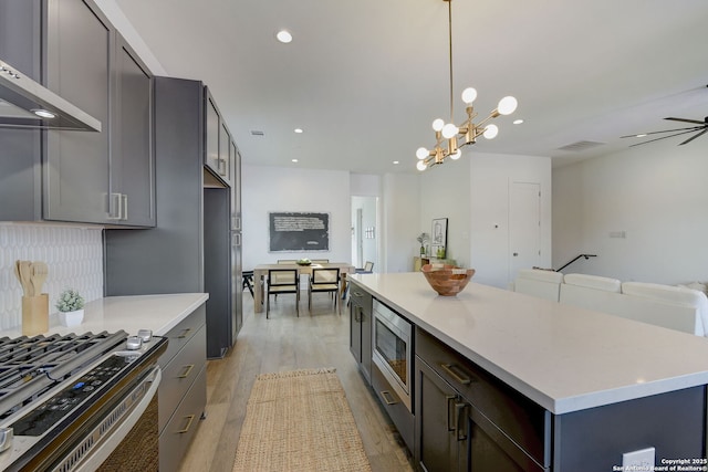 kitchen featuring built in appliances, a center island, pendant lighting, light hardwood / wood-style floors, and wall chimney range hood