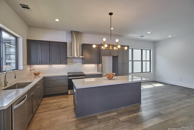 kitchen with wall chimney exhaust hood, sink, a center island, appliances with stainless steel finishes, and pendant lighting