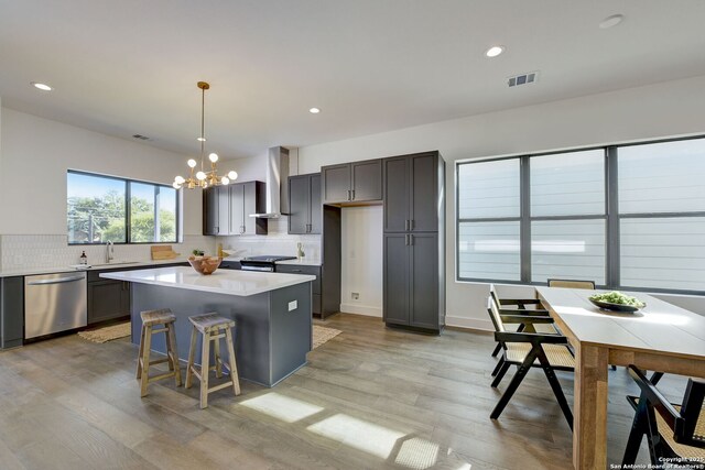 kitchen featuring a center island, hanging light fixtures, stainless steel appliances, decorative backsplash, and wall chimney range hood