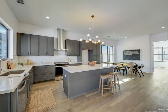 kitchen with pendant lighting, sink, a center island, stainless steel appliances, and wall chimney range hood