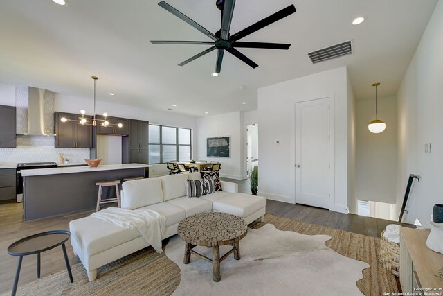 living room featuring ceiling fan with notable chandelier and light hardwood / wood-style floors