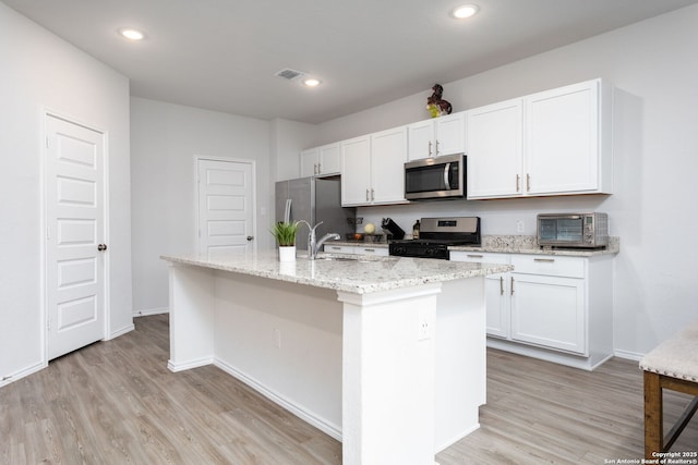 kitchen featuring appliances with stainless steel finishes, white cabinetry, light stone counters, light hardwood / wood-style floors, and a center island with sink