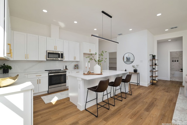 kitchen with a center island, light wood-type flooring, pendant lighting, stainless steel appliances, and white cabinets