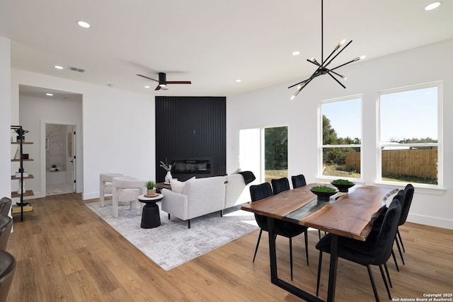 dining space with ceiling fan with notable chandelier and light wood-type flooring