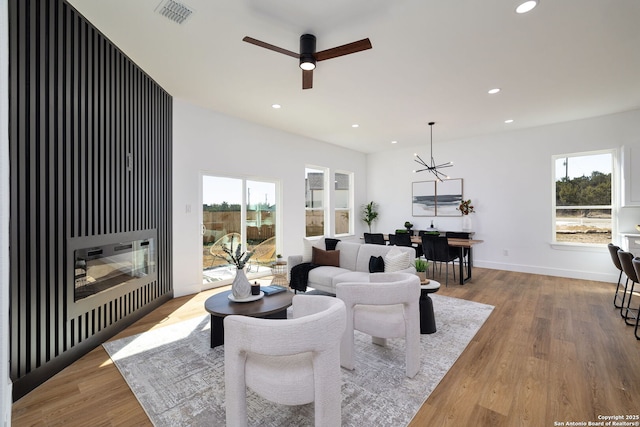 living room featuring ceiling fan with notable chandelier and light hardwood / wood-style flooring