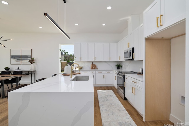 kitchen with appliances with stainless steel finishes, decorative light fixtures, sink, white cabinets, and light stone countertops