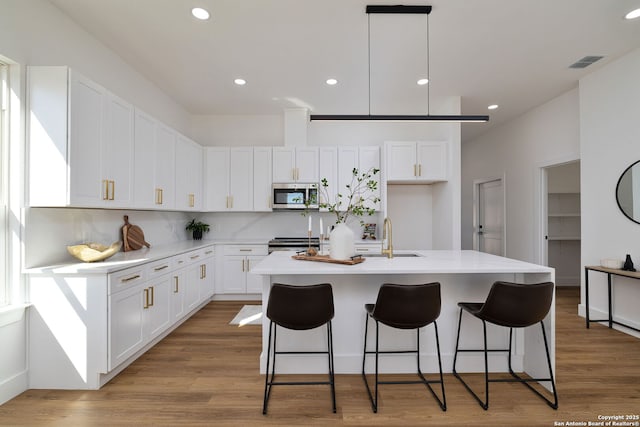 kitchen with appliances with stainless steel finishes, white cabinetry, an island with sink, sink, and light hardwood / wood-style floors