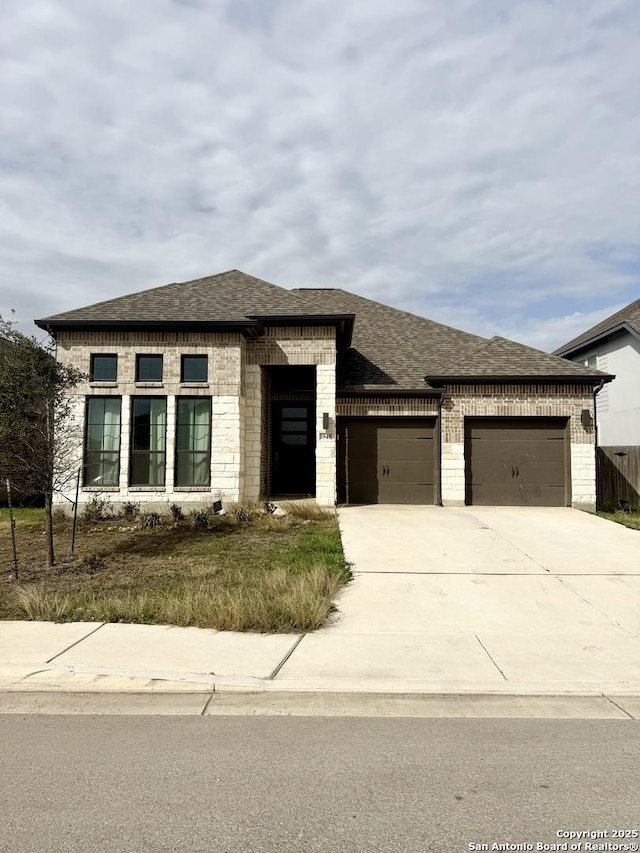 view of front facade with a shingled roof, brick siding, driveway, and an attached garage