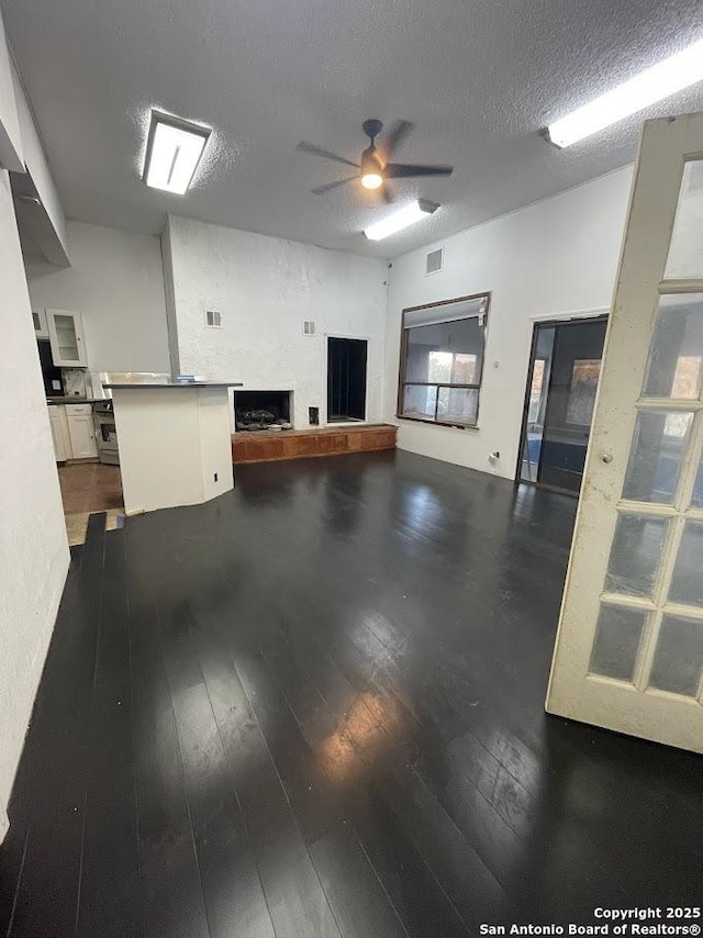 unfurnished living room with ceiling fan, dark wood-type flooring, and a textured ceiling