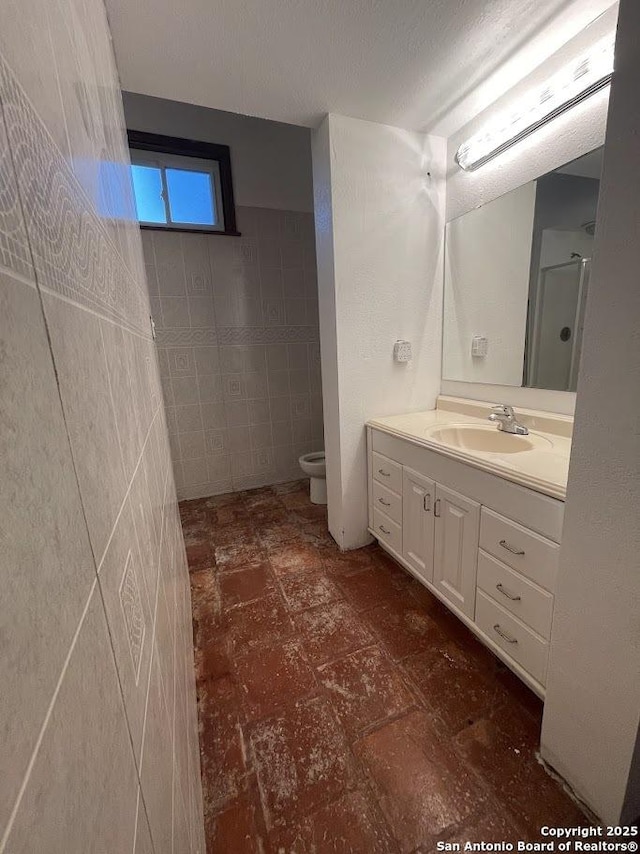 bathroom with vanity, tile walls, and toilet