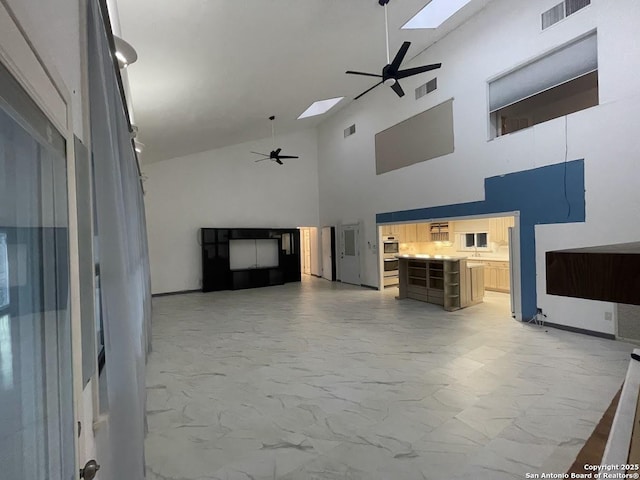 unfurnished living room with high vaulted ceiling, ceiling fan, and a skylight