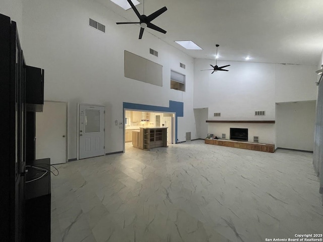 unfurnished living room featuring a towering ceiling, a fireplace, ceiling fan, and a skylight